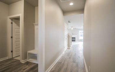 Family Entry | Hall to Family Room Family Entry and hallway in the Emory Craftsman floor plan by Jagoe Homes, leading to the Family Room with a view of the fireplace and staircase to the bonus room