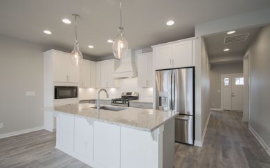 Foyer | Kitchen w/ Deluxe Features Deluxe features Kitchen with range hood and microwave cabinet in the Emory Craftsman floor plan by Jagoe Homes, offering a view into the foyer with sightlines to the staircase leading to the bonus room