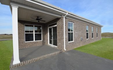 Outdoor Retreat Rear exterior of the Emory Craftsman floor plan by Jagoe Homes, showcasing a covered patio with a ceiling fan, brick siding, sliding glass doors, and large windows for natural light and outdoor living.