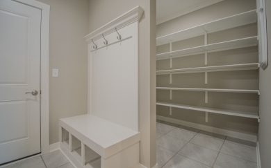 View of a family entry drop zone with a built-in bench, cubbies, and coat hooks adjacent to a spacious walk-in pantry with multiple white shelves.