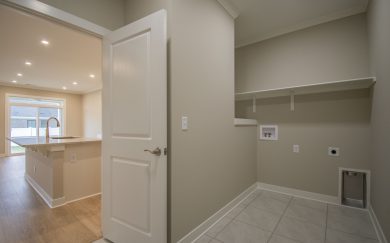 Laundry room with tile flooring, upper shelf, and utility hookups, located adjacent to an open-concept kitchen with island and backyard access.