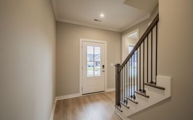 Interior view of a home entryway with Revwood flooring, a white front door with glass panel, and a staircase with wooden handrail and black metal balusters.