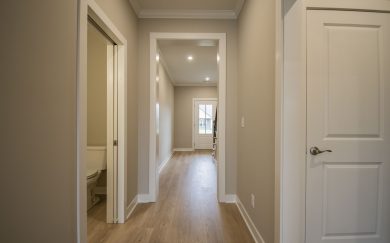 A view from the hallway in the Little Rock Craftsman showing warm Revwood flooring, a half bath to the left, and the front door and staircase in the distance.