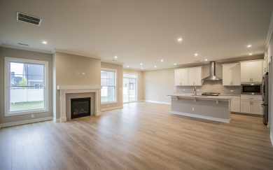 Open-concept living area with Revwood flooring, LED lighting, a white fireplace, and a modern kitchen featuring white cabinets, a large island, and a stainless steel hood.