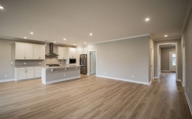 Spacious open kitchen and living area with wide plank Revwood flooring, white cabinetry, stainless steel appliances, and LED lighting.