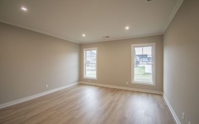 Spacious owner's bedroom with warm Revwood flooring, two large windows for natural light, and neutral wall tones.
