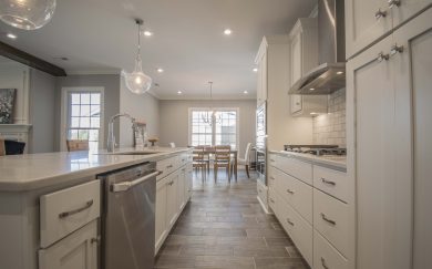 Modern kitchen with white cabinetry, stainless steel appliances, a large center island with pendant lighting, and a view into a dining area with natural light from a large window.