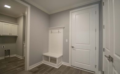 Family Entry with built-in bench and cubbies, coat hooks, and a view into an adjacent laundry room featuring upper cabinetry and tile flooring.