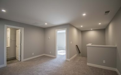 Upstairs loft area with neutral carpeting, LED lighting, access to a full bathroom, and two bedrooms, with stairway access visible on the right.