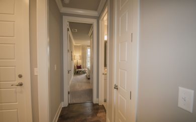 Hall to Bedrooms | Bath Hallway in the Merlot floor plan leading to a secondary bedroom with a cozy reading nook and a window offering natural light. The hallway also features access to a bathroom and linen closet, with warm wood flooring and neutral tones.