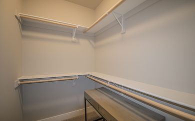 Secondary Bedroom Closet Spacious walk-in closet in the Merlot floor plan featuring double hanging rods and upper shelving for ample storage. A small wood console adds functionality and style.