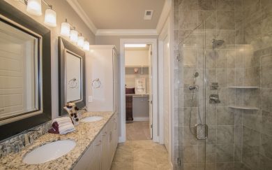 Owner's Bath | Closet Primary bathroom in the Merlot floor plan featuring a double vanity with granite countertops, a glass-enclosed walk-in shower with tile surround, and a spacious walk-in closet. Elegant lighting and modern fixtures complete the space.