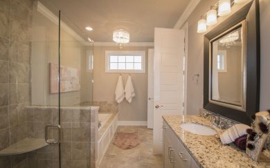 Owner's Bath Luxurious primary bathroom in the Merlot floor plan, featuring a large walk-in shower with glass enclosure, a soaking tub with tile surround, and a granite-topped vanity with elegant lighting. A chandelier adds a touch of glamour, while neutral tones and soft accents create a relaxing atmosphere.