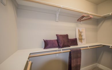 Owner's Closet Spacious walk-in closet in the Merlot floor plan featuring built-in shelving, double hanging rods, and a neutral color palette. Decorative pillows, a cozy throw, and an inspiring “Make Today Amazing” sign add a personal touch.
