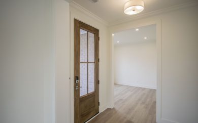 Foyer | Home Office Interior view of the Malbec home’s entryway showcasing a wood look glass front door, crisp white walls, and Revwood flooring leading into a bright home office.