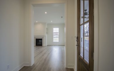 Foyer | Great Room View from inside the Malbec home entryway looking into the great room, showcasing a wood look framed glass front door, light Revwood, and a white-painted fireplace with trim detailing.