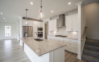 Kitchen | Stairs to Second Floor Spacious modern kitchen in the Malbec floorplan featuring a large quartz island with double bowl sink, white cabinetry, stainless steel appliances, and a sleek tile backsplash.