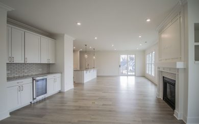 Great Room | Beverage Center | Dining Area Spacious view of the Malbec’s great room featuring a fireplace with detailed millwork, built-in cabinetry with a beverage cooler, and a large kitchen island illuminated by pendant lighting.