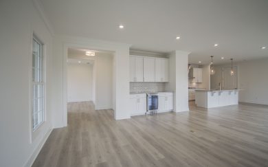 Great Room | Beverage Center | Kitchen View of the open-concept living space in the Malbec floorplan, showcasing a built-in beverage center, white cabinetry, pendant lighting over the kitchen island, and wide plank Revwood flooring.