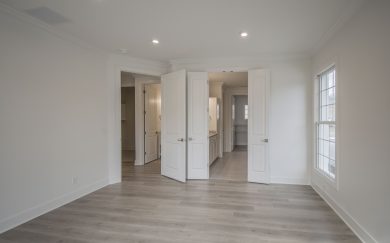 Owner's Suite Owner's suite with open double doors leading to a spacious en-suite bathroom and walk-in closet, featuring large windows and Revwood flooring.