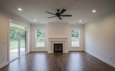 Living room in the Emory Craftsman featuring Revwood flooring, a white subway tile surround fireplace centered between two large windows, a ceiling fan, and sliding glass doors leading to the covered patio and backyard.