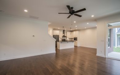 Spacious open-concept living area in the Emory Craftsman home, featuring Revwood flooring, a ceiling fan, view of the kitchen with island and pendant lights, and sliding glass doors leading to the covered patio and backyard.