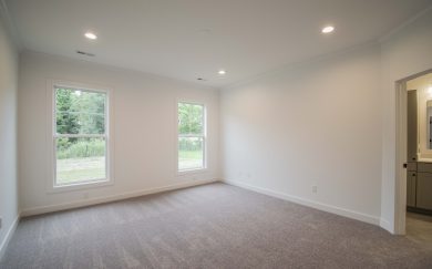 Spacious owner&rsquo;s suite with plush carpet, two large windows bringing in natural light, led ceiling lights, and an entrance to the private en suite bathroom.