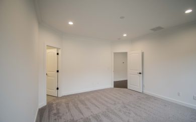 Interior view of the owner&rsquo;s suite featuring soft carpeting, led lighting, and two open doorways&mdash;one leading to the en suite bathroom and the other to the main living area.