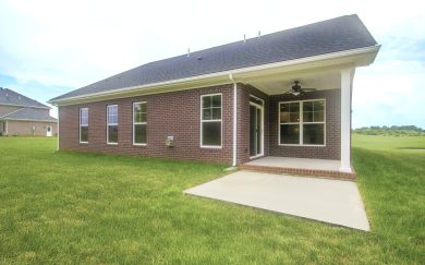 Back exterior view of the Emory Craftsman home showcasing a full brick fa&ccedil;ade, covered back patio with ceiling fan, and open concrete extension surrounded by a grassy backyard.
