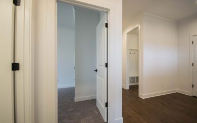 View of a hallway in the Emory Craftsman home, showing a doorway to a carpeted bedroom, revwood flooring, and a built-in drop zone with coat hooks and cubbies.