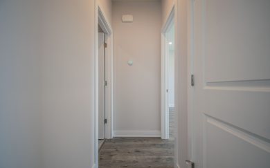 View down a hallway in the Leonardo Craftsman home, showing entryways to the laundry room and owner&rsquo;s suite with luxury vinyl plank flooring and soft neutral walls.