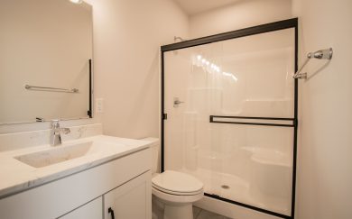 Modern bathroom featuring a white countertop vanity, chrome fixtures, and a large walk-in shower with sliding glass doors and black trim.