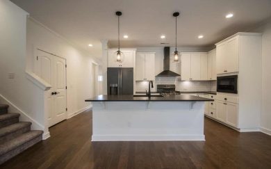 Deluxe kitchen in the Emory Craftsman home with white shaker cabinets, black countertops, a subway tile backsplash, stainless steel appliances, and two glass pendant lights above the island.