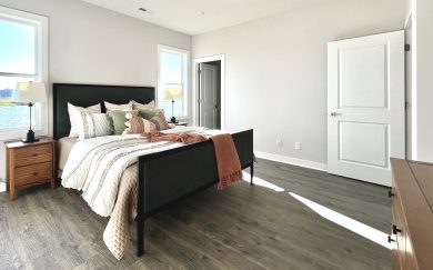 Owner&rsquo;s suite in the Leonardo Craftsman featuring Revwood flooring, large windows with lake views, and neutral-toned decor.