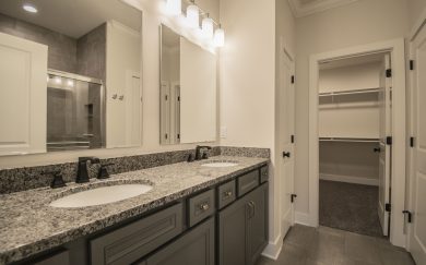 Owner&rsquo;s Bath with a double bowl vanity with granite countertops, a ceramic walk-in shower, and an Owner&rsquo;s Closet with MDF shelving in the Arizona Craftsman floor plan by Jagoe Homes.
