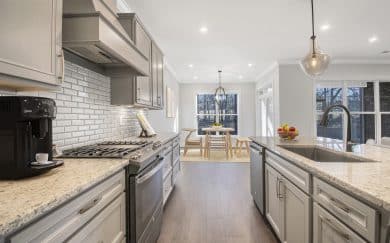 Deluxe Kitchen | Dining Area Modern kitchen with gray cabinets, stainless steel appliances, a gas cooktop, coffee station, white subway tile backsplash, and a central island with pendant lighting and a sink.