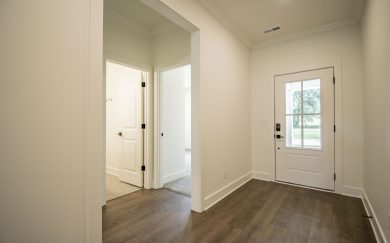Foyer | Hall to Bedrooms and Bath View of a bright and welcoming entryway with Revwood flooring, a white front door with glass panes, and access to interior rooms with neutral carpet and tile finishes.