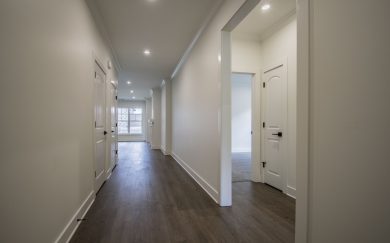 Foyer | Hall to Bedrooms & Bath | Optional Bedroom 3 in lieu of Flex Space Long hallway with Revwood flooring, soft white walls, led lighting, and multiple doorways leading to bedrooms and living areas.