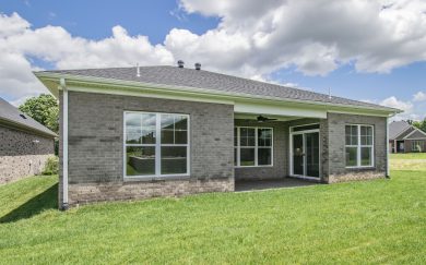 Outside Retreat Rear exterior view of a brick home showcasing large windows and a covered patio with ceiling fan, overlooking a grassy backyard.